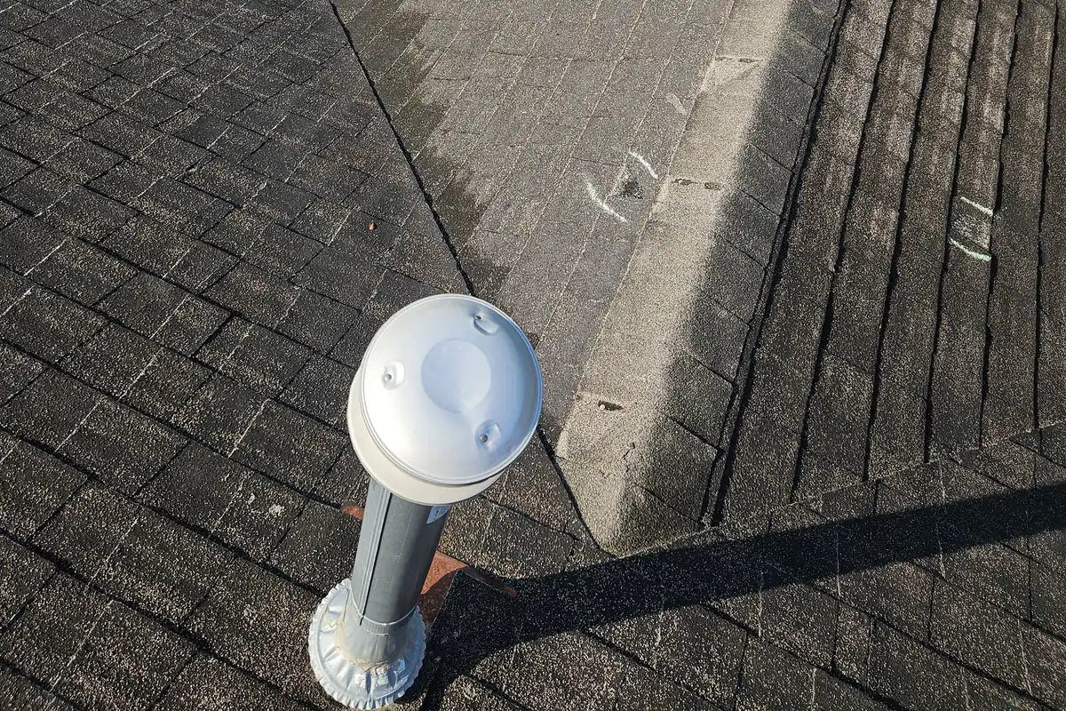 Metal vent pipe and flashing beside asphalt shingles.