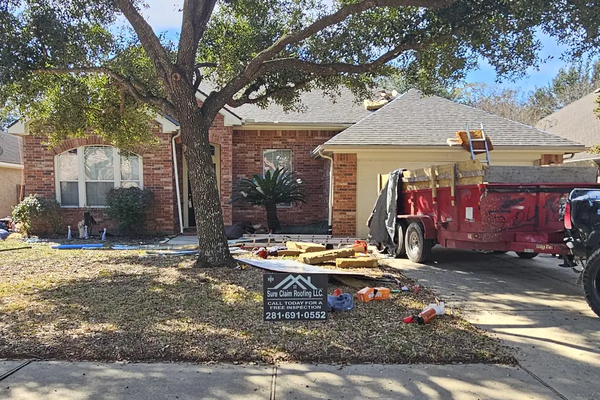 Roofing materials and a debris trailer beside a house during roof work.
